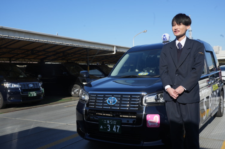 大和自動車交通株式会社の若手ドライバーが停まっているタクシーの前で姿勢を正して立っている様子
