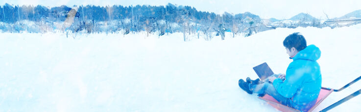 雪景色の中橇の上でPC作業をするドコドア株式会社のメンバー