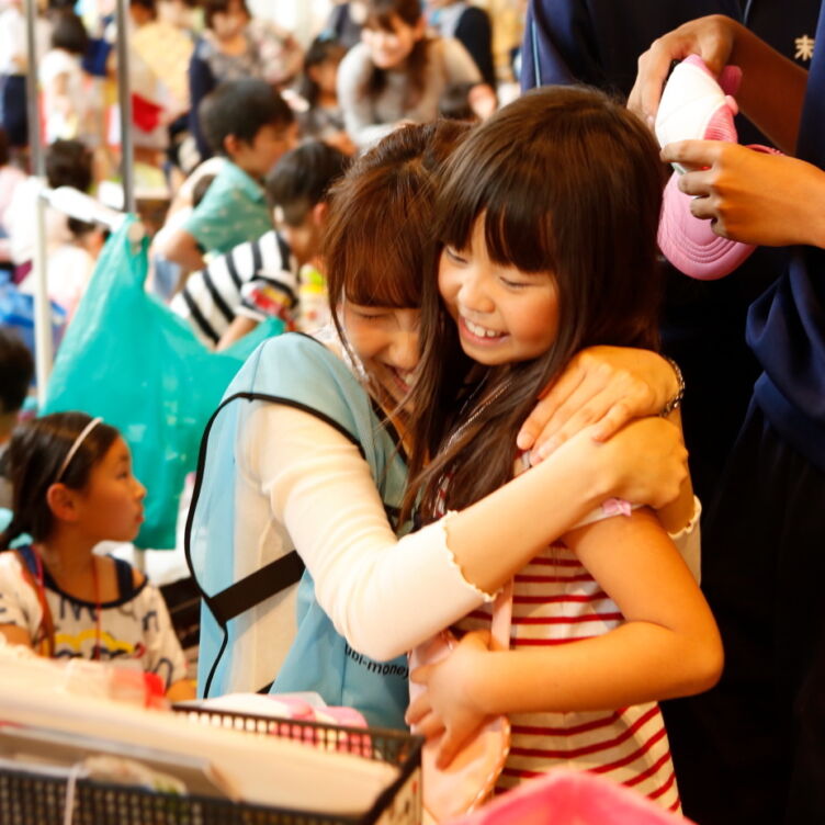 一般社団法人ユメ・フルサトが運営する「こども夢の商店街」で、子どもと抱き合う学生ボランティア