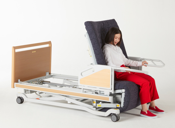 フランスベッド株式会社が介護ベッドとして開発されたマルチポジションベッドに人が腰を掛けて使用している様子