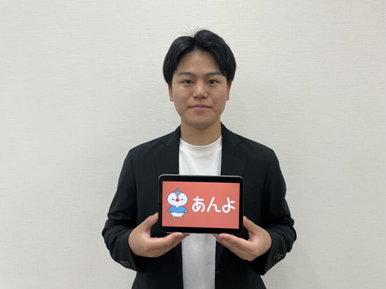 ジークス株式会社代表取締役CEOの村上嘉一さんが「あんよ」のロゴが表示されたタブレットを持つようす