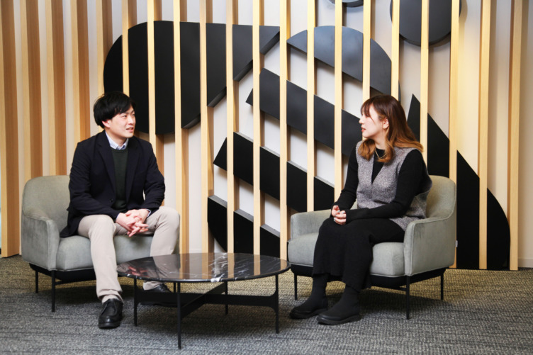 日本アイ・ビー・エムデジタルサービス株式会社の社内にあるソファで談笑する佐竹さんと戸塚さん
