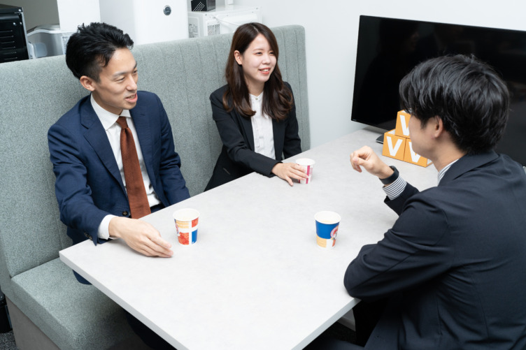 株式会社ブイキューブの社員3名が机を囲んで飲み物を飲みながら談笑している様子