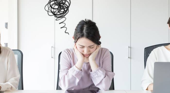 女性が椅子に座って頬に手をついて悩んでいる姿