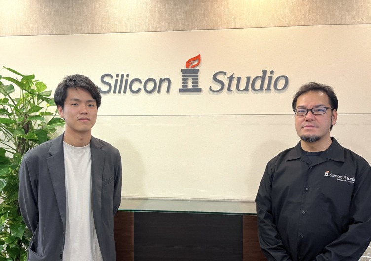 シリコンスタジオ株式会社の向井さんと江森さんが会社ロゴの前に並んで立つようす