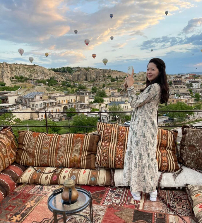 ベルトラ株式会社の女性社員が滞在先のトルコで気球を背景に記念写真を撮るようす